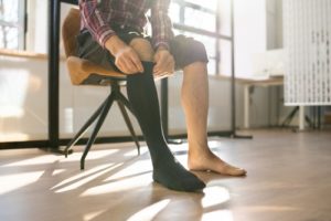 Man Putting On Medical Compression Stockings On Legs